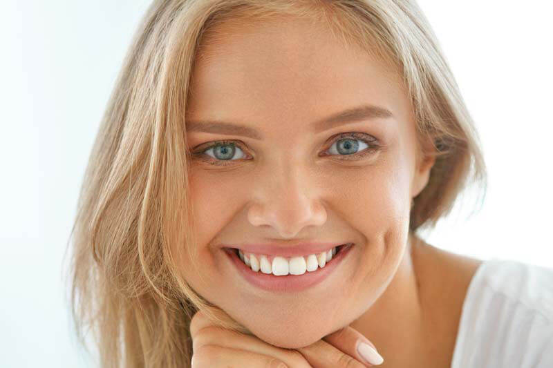 Close-up picture of a smiling woman with long blonde hair, happy with her dental veneers she had at Premier Holistic Dental in Costa Rica.