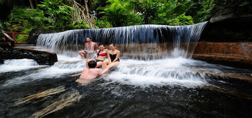 Picture of visitors to a natural waterfall in a Costa Rica Hot Springs spa while having dental work at Premier Holistic Dental in beautiful Costa Rica. The picture is of four tourists sitting in a pool formed by the hot springs waterfall depicting the vacation opportunities of having dental work at Premier Holistic Dental in Costa Rica. 
