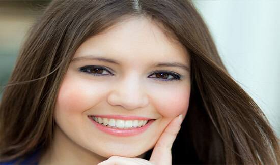 Close-up picture of a smiling woman with long brown hair and perfect teeth, looking directly at the camera and showing her happiness with the all-on-two dental treatment she had at Premier Holistic Dental in beautiful Costa Rica.