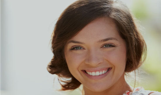 Close-up portrait picture of a smiling woman with short brown hair and with perfect teeth, looking directly at the camera and showing her happiness with the dental crowns she had at Premier Holistic Dental in beautiful Costa Rica.