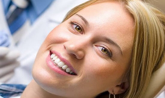 Picture of a smiling woman with long blonde hair and perfect white teeth,  in a dental chair and facing the camera, showing her happiness with the dental implants she had at Premier Holistic Dental in beautiful Costa Rica.