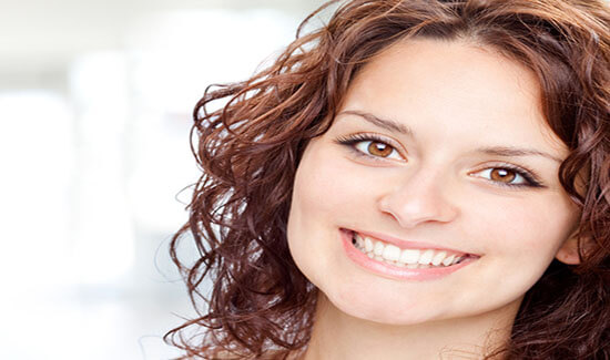 Close-up portrait picture of a smiling woman with long brown hair and with perfect teeth, looking directly at the camera and showing her happiness with the full mouth makeover she had at Premier Holistic Dental in beautiful Costa Rica.