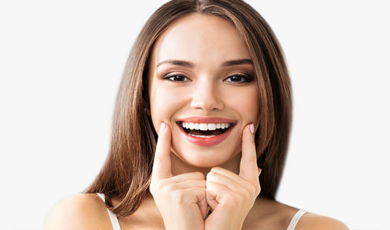 Portrait picture of a smiling woman with long brown hair, holding two fingers up to the sides of her face, looking at the camera and showing her happiness with the dental inlays and onlays she had at Premier Holistic Dental in beautiful Costa Rica.