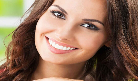 Close-up picture of a smiling woman with long brown hair and perfect teeth, looking directly at the camera with her head slightly tilted, showing her happiness with the Invisalign dental treatment she had in Costa Rica.
