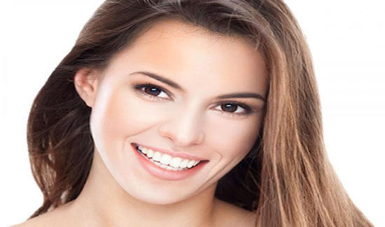 Close-up portrait picture of a smiling woman with long brown hair and with perfect teeth, looking directly at the camera and showing her happiness with the prosthodontics procedure she had in Costa Rica.