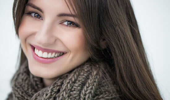 Close-up portrait picture of a smiling woman with long brown hair and perfect teeth, looking directly at the camera and illustrating her happiness with the safe mercury removal procedure she had at Premier Holistic Dental in beautiful Costa Rica.