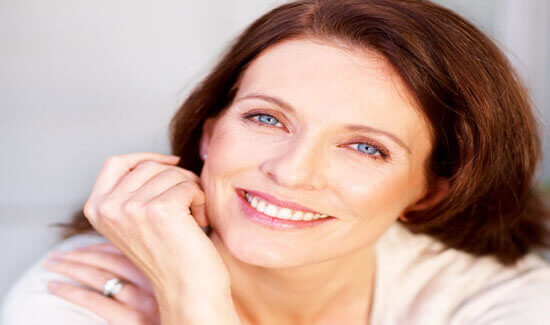 Close-up picture of a smiling woman with long brown hair, wearing a white blouse and looking directly at the camera, illustrating her happiness with the sinus lift treatment she had at Premier Holistic Dental in beautiful Costa Rica.