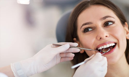 Close-up picture of a young woman sitting in a dental chair having her teeth cleaned at Premier Holistic Dental in beautiful Costa Rica.  A dentist is holding dental implements showing how Holistic dental cleaning is done by Premier Holistic Dental.