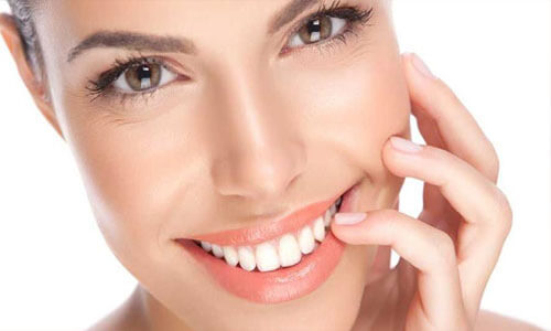 Close-up picture of a smiling young woman, holding her hand to her face to show perfect white teeth, and happy with her Holistic dental extractions treatment at Premier Holistic Dental in beautiful Costa Rica.