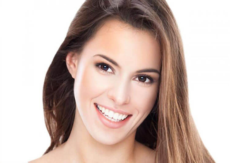 Picture of a smiling woman with long brown hair, happy with implant-supported bridge she had at Premier Holistic Dental in Costa Rica.