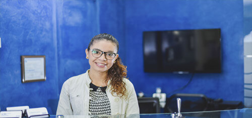 Picture of a receptionist at Premier Holistic Dental in San José, Costa Rica.  The receptionist is sitting in a chair, facing the camera, and smiling warmly at the camera.